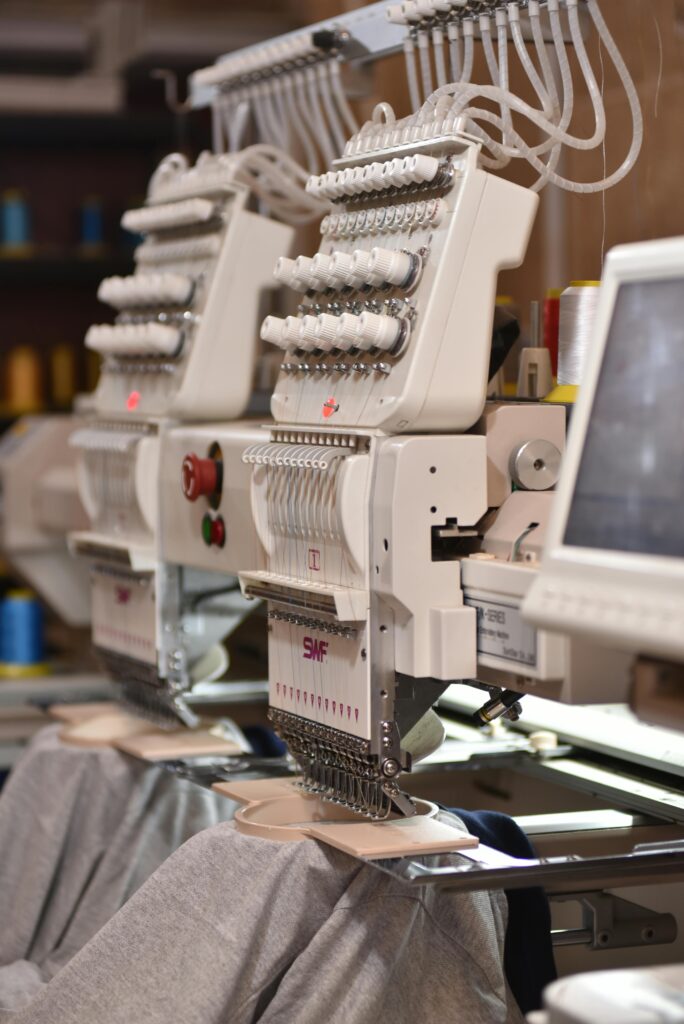 Close-up of automated industrial sewing machines stitching fabric in a factory setting.